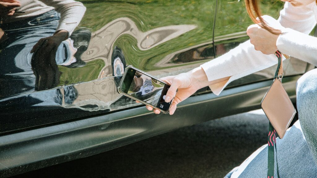 close up of hand of young lady holding mobile phone squatting down near damaged door of car and tak.jpeg